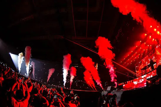 Plateia lotada com jatos de fumaça vermelha durante o show