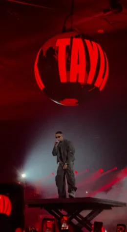 Veigh no palco sob uma esfera vermelha com a palavra Taylor